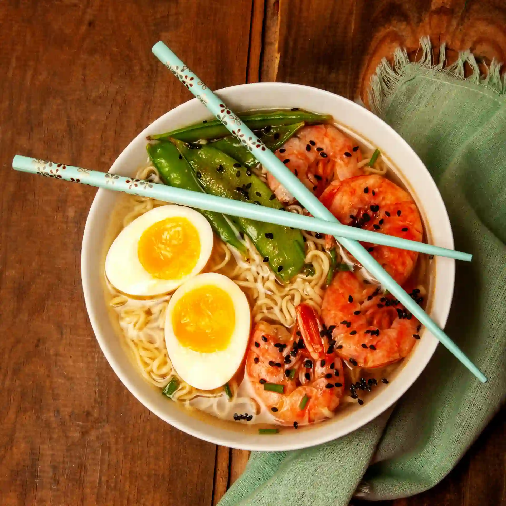 Overhead view of a Japanese ramen bowl with shrimp, soft-boiled egg, and snap peas